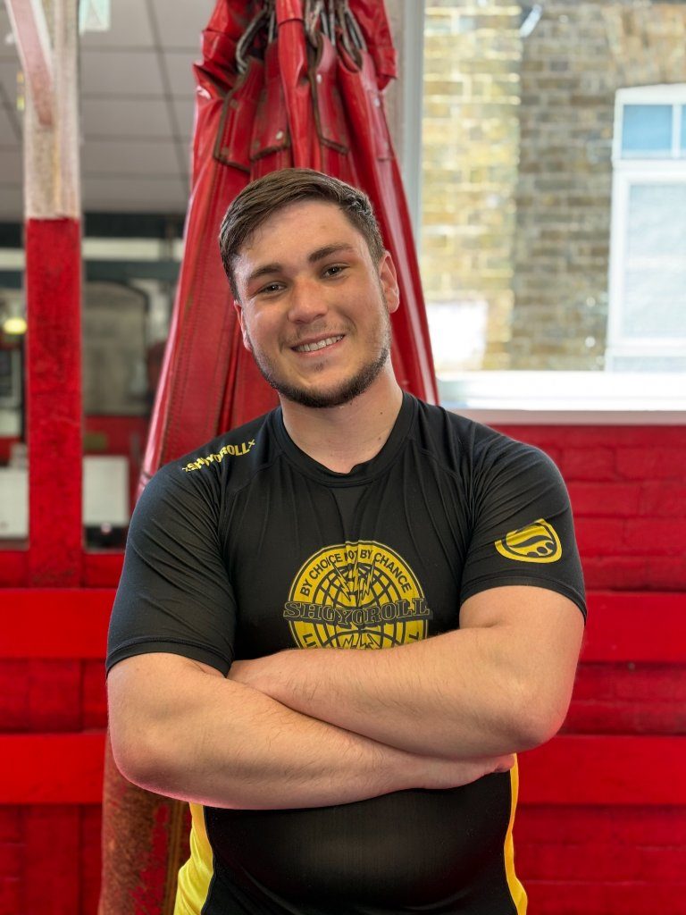 Jordan Cogan smiling with his arms folded in front of a red heavy bag in the gym