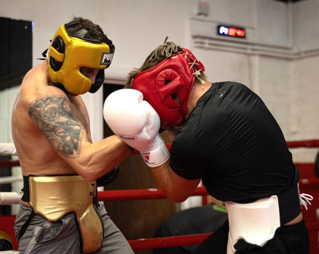Two boxers sparring in headguards, one in a gold headguard and one in red
